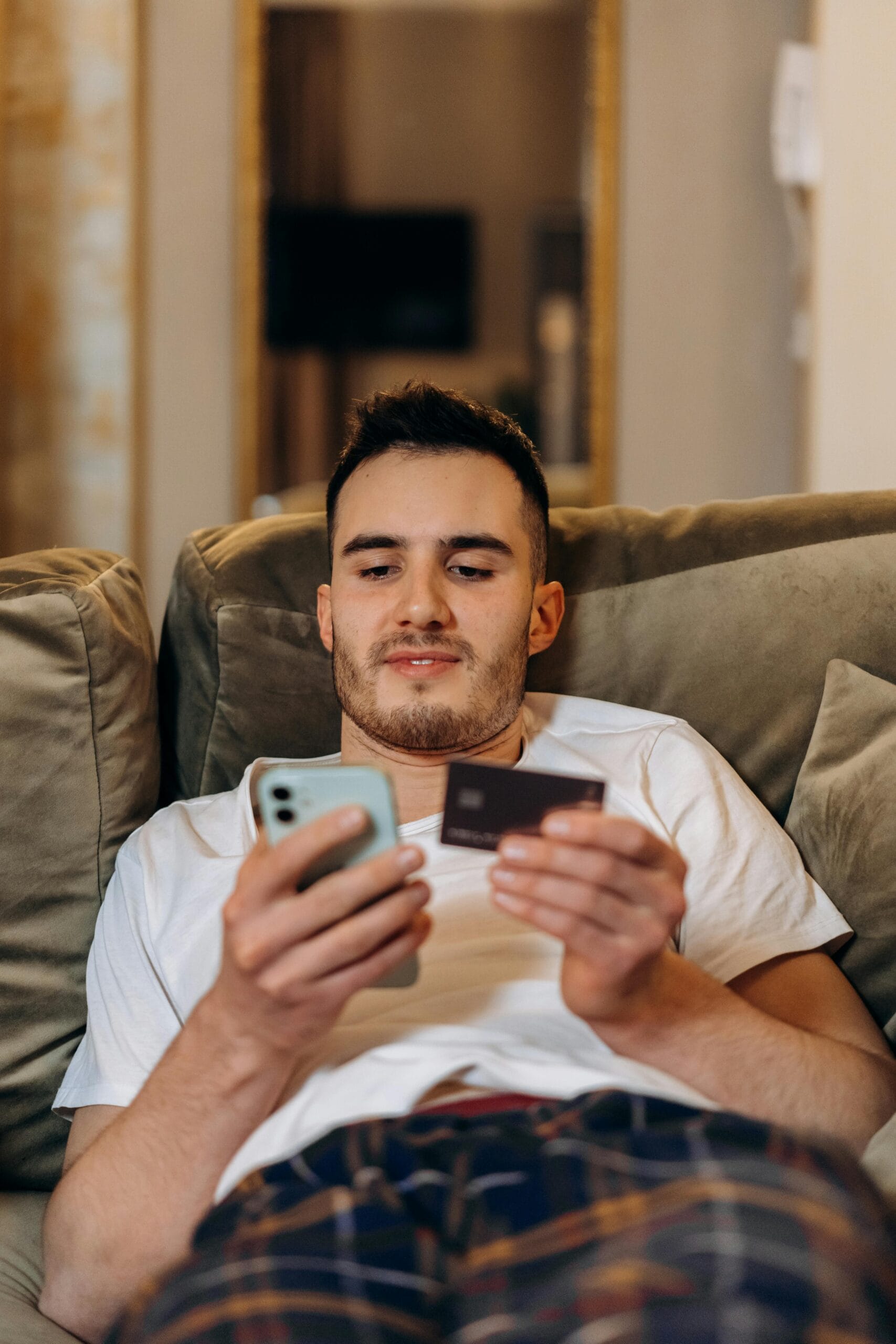 Young man using smartphone and credit card for online shopping indoors.